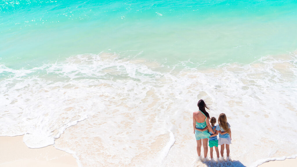 A Mother and Her Two Daughters Enjoy the Turquoise Waves and Soft White Sand Of Grace Bay Beach